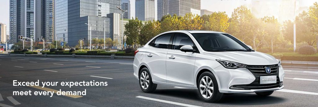 سيارة سيدان Changan Alsvin بيضاء من زاوية أمامية جانبية على طريق في المدينة مع ناطحات سحاب زجاجية في الخلفية