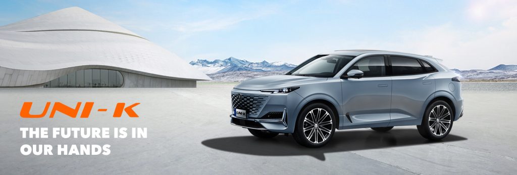 سيارة Changan UNI-K فضية SUV بزاوية أمامية جانبية مع مبنى أبيض مستقبلي وجبال في الخلفية